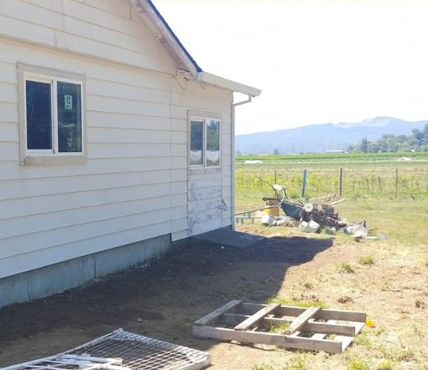 Rural farmhouse with white siding under construction, surrounded by fenced pasture and mountains