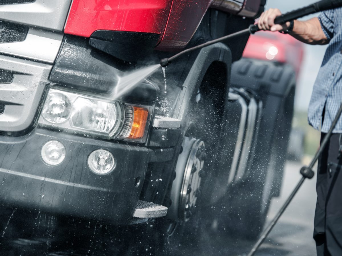 Person pressure washing black SUV with high-pressure water spray